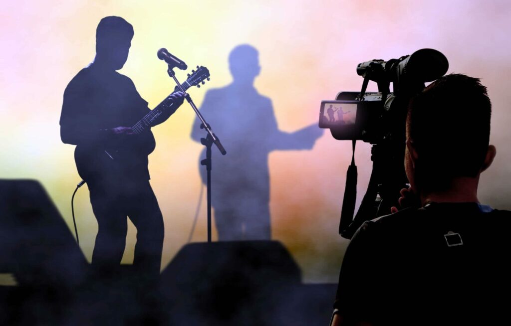 Cameraman recording and broadcasting live concerts on on stage using video camera.
