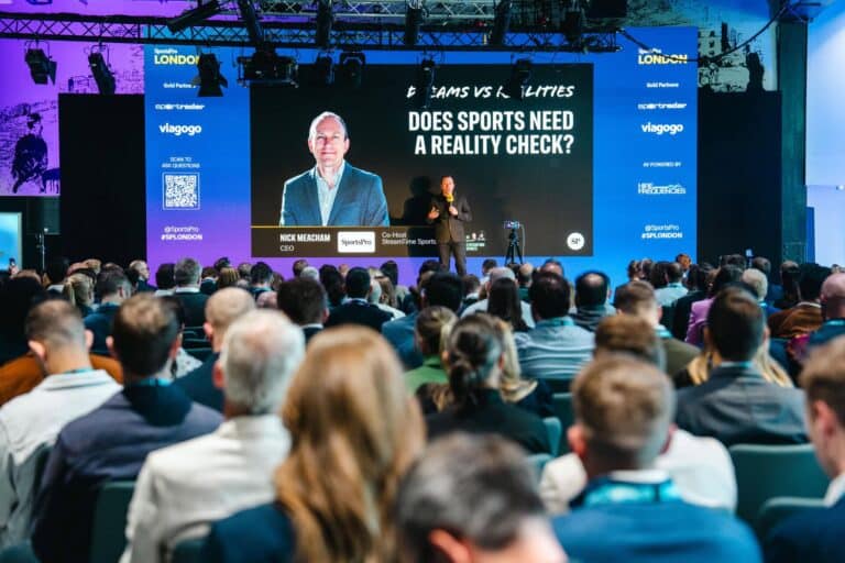Speaker presenting “Does sports need a reality check?” to a seated audience at a SportsPro conference.